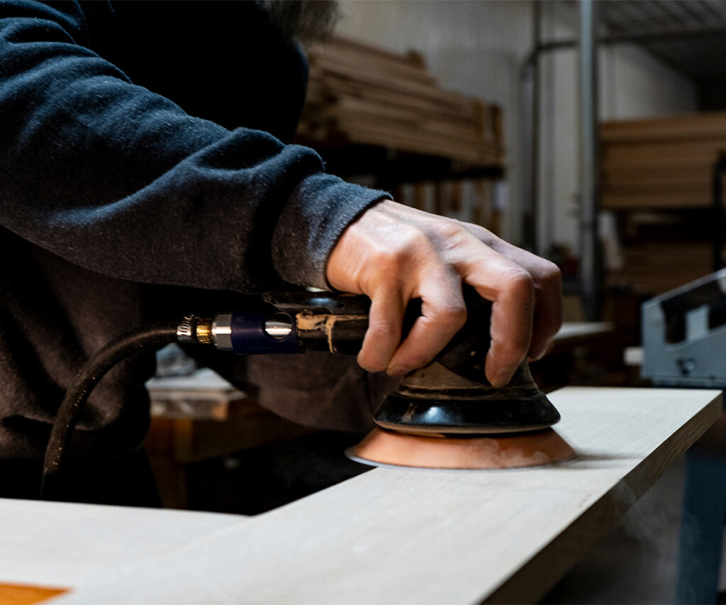 Amish craftsman sanding local Amish furniture tabletop edge