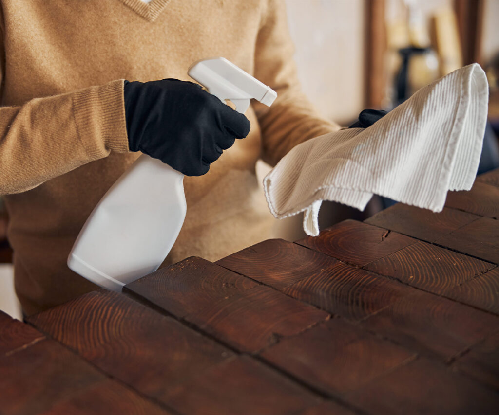 Gloved hands spraying and wiping a solid wood tabletop