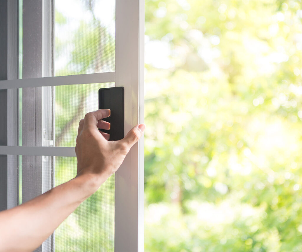 Hand opening a window screen with bright outdoor light behind it