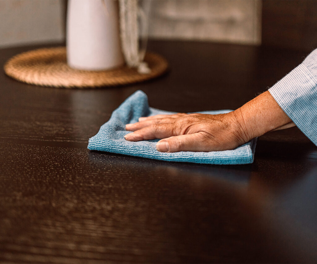 Hand wiping dark wood furniture with a blue microfiber cloth